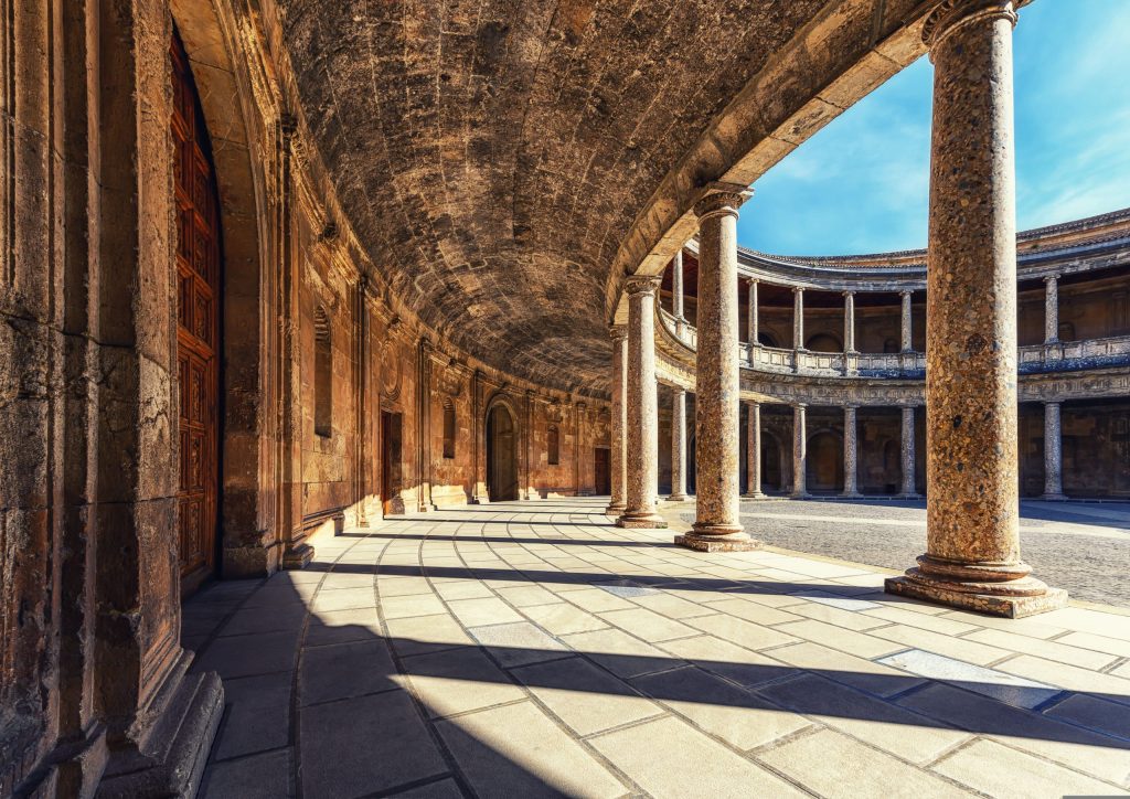 Interior view of a round stone courtyard with columns casting shadows.