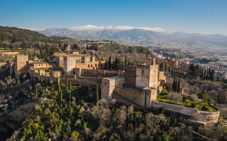 Aerial view of a historic fortress with mountains in the background.