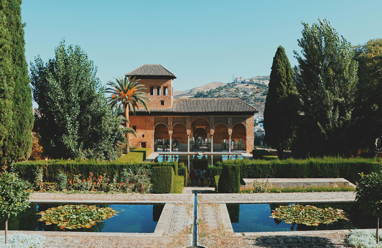 Historic building with arches, surrounded by lush gardens and water features.