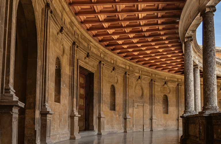 Curved stone colonnade with arches and wooden ceiling.
