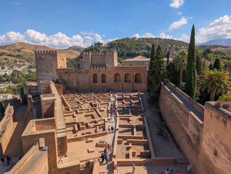 Aerial view of Alhambra fortress with people exploring its stone courtyard.