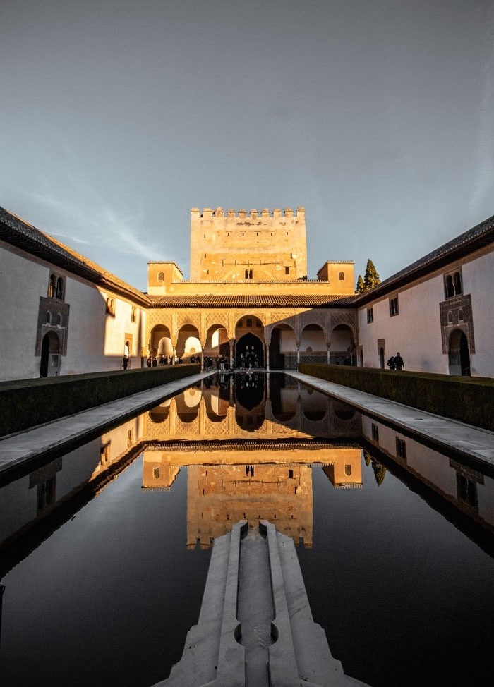 Symmetrical view of a castle reflected in a long pool at sunset.