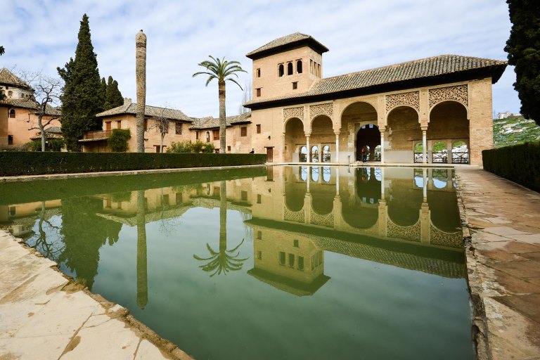 Historic Moorish building with arches, reflected in a long pool.