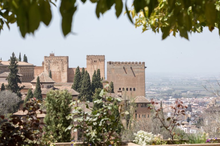 Historic castle with towers, surrounded by trees, with a cityscape in the background.