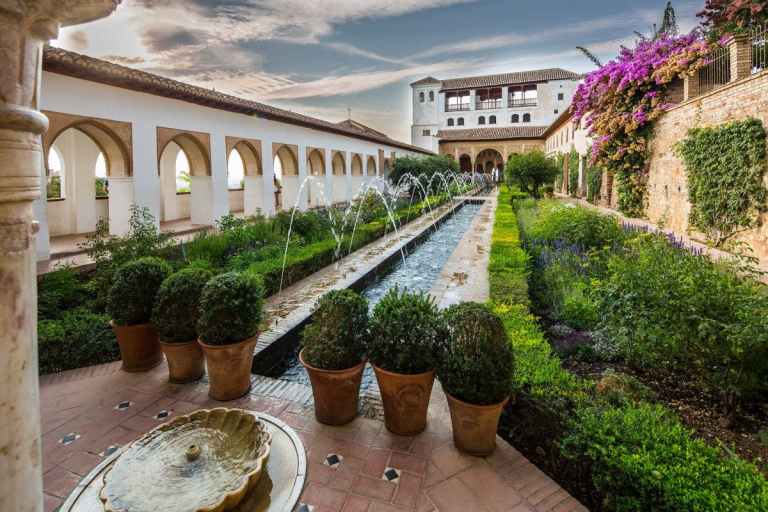 Historic garden courtyard with arched walkway, fountain, and flowers.