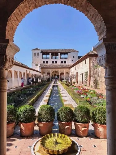 Arched view of garden with fountain and historic building under clear blue sky.