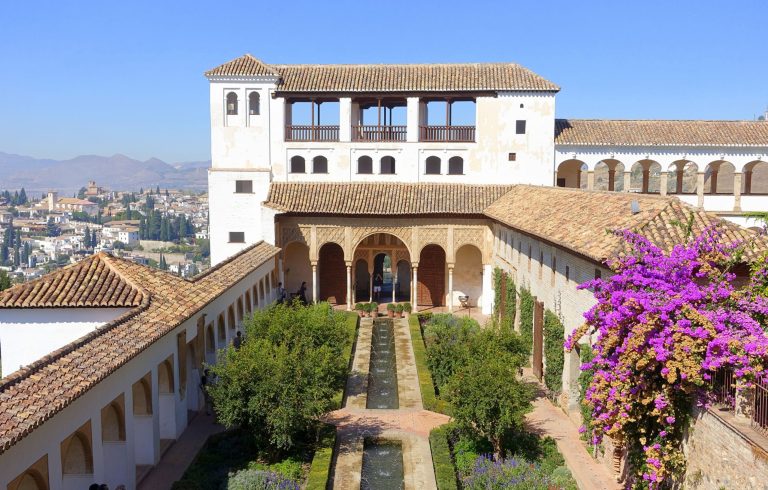 Historic courtyard with arches, gardens, and vibrant bougainvillea.