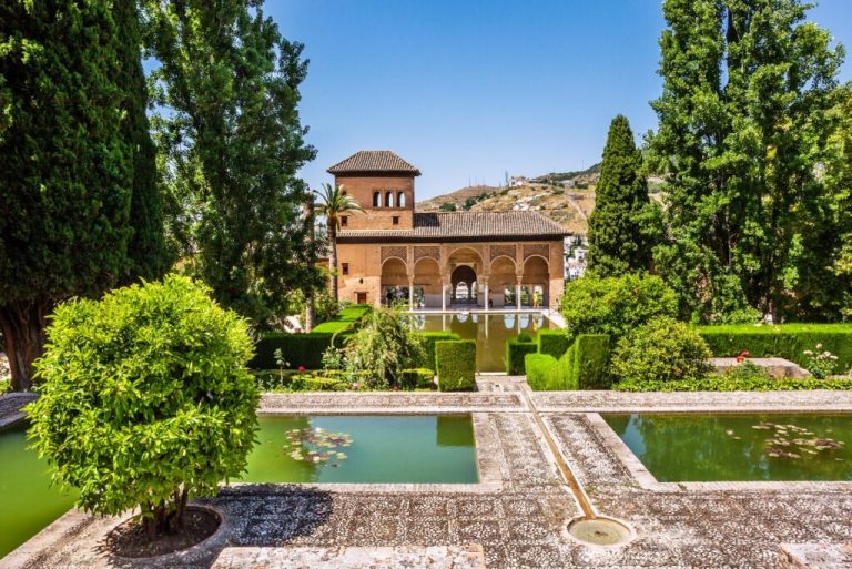 Historic building with gardens, ponds, and trees in a sunny setting.