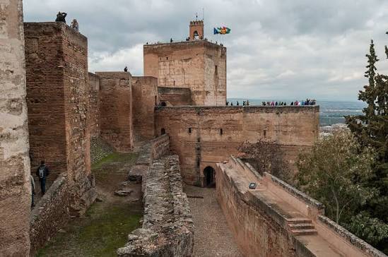 Stone fortress with tower, people on walls, cloudy sky.